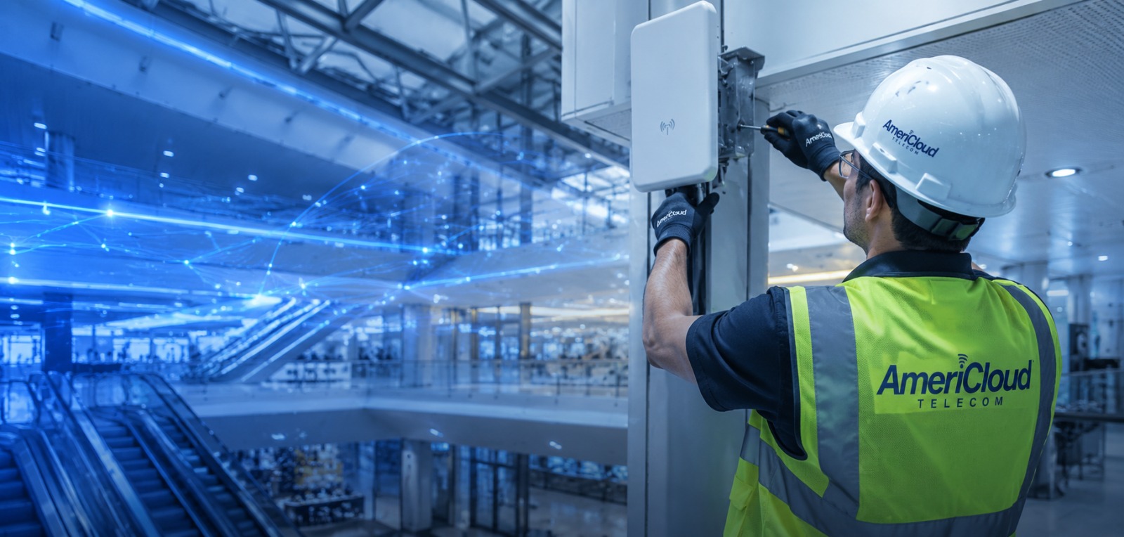 AmeriCloud technician in branded vest and hard hat installing a wireless antenna, with signal arcs over a venue concourse