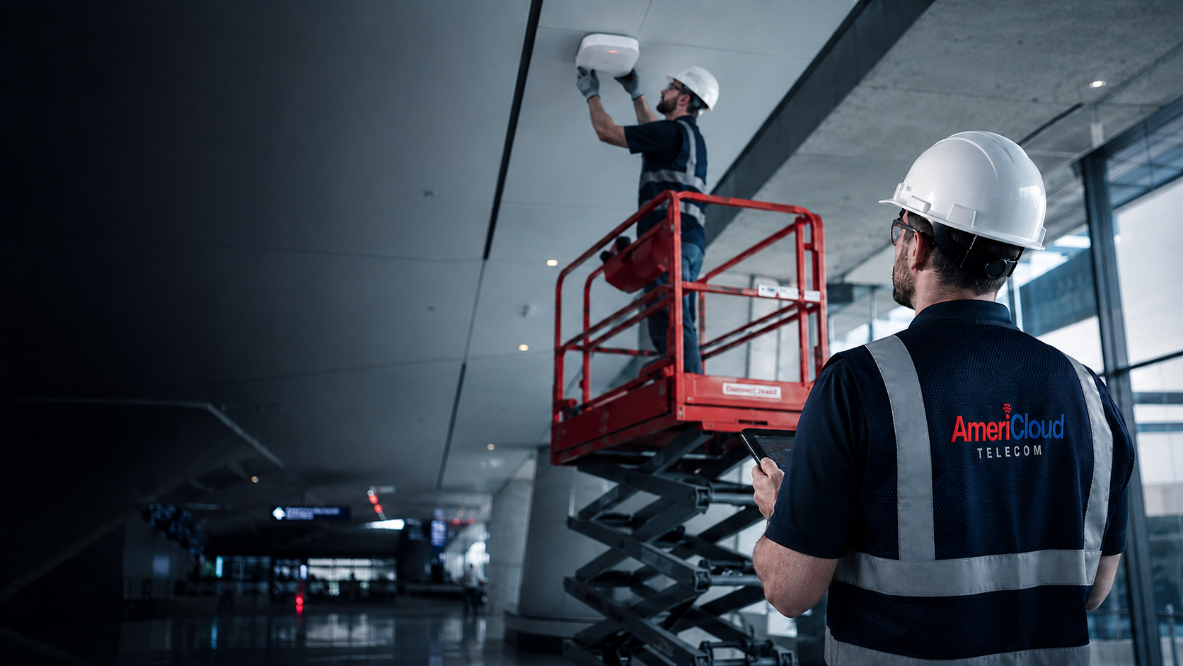 AmeriCloud technicians installing a ceiling DAS antenna from a lift inside a modern venue concourse